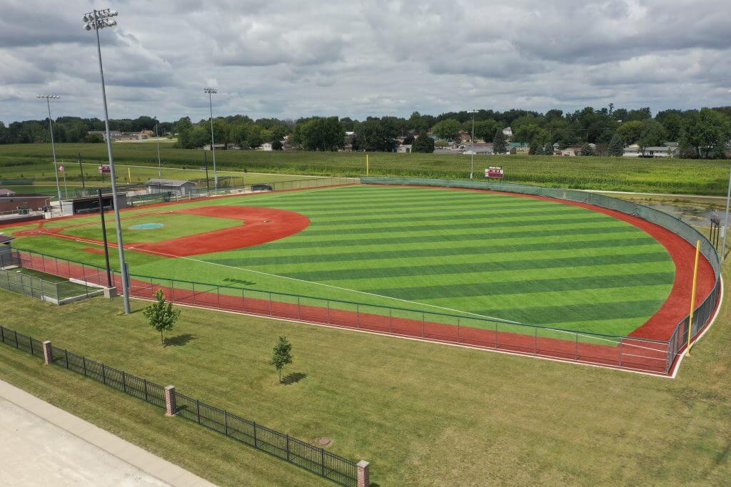 Aerial view of the Independence Community School District baseball field featuring a turf infield and grass outfield, with visible improvements to address drainage issues.